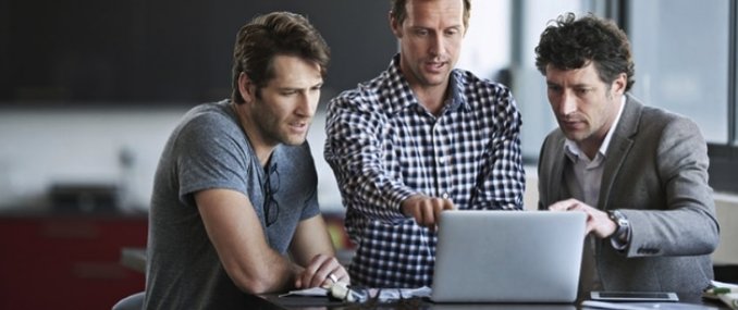 Männliche Mitarbeiter stehen vor einem Laptop, der mit Cloud App Security geschützt ist